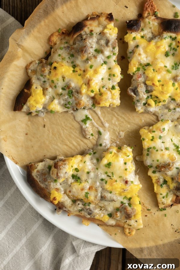 A partially assembled Sausage Gravy Breakfast Pizza, showing scrambled eggs spread over a crust and dollops of sausage gravy being added.