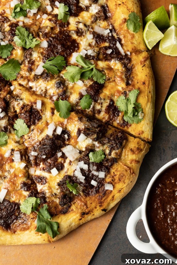 A Birria Pizza with tender shredded beef, melted cheese, cilantro, and lime, served with dipping sauce.