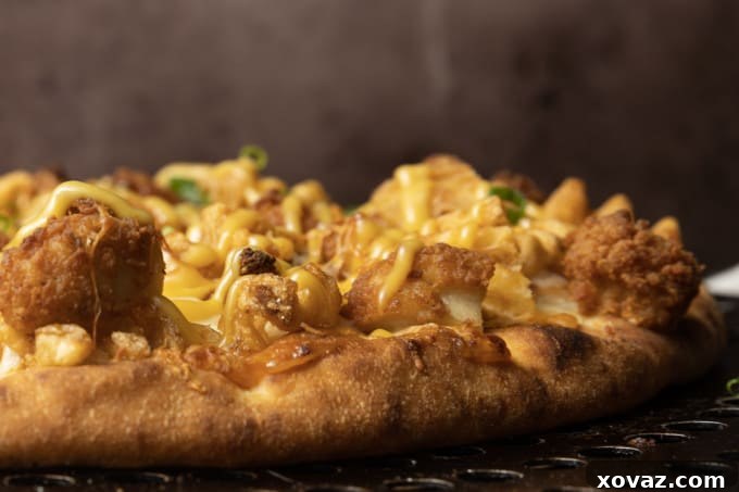 Close-up of a slice of Chick-fil-A Pizza showing melted cheese, golden chicken nuggets, and crispy waffle fries on a rich sauce base.