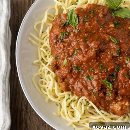 spaghetti sauce on spagetti on a plate topped by fresh herbs with a napkin and fork on the left.