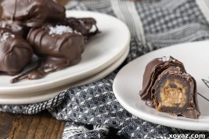 Cross-cut almond butter stuffed Medjool dates covered in dark chocolate and sprinkled with flaky sea salt, arranged on small white plates with a blue and white linen.