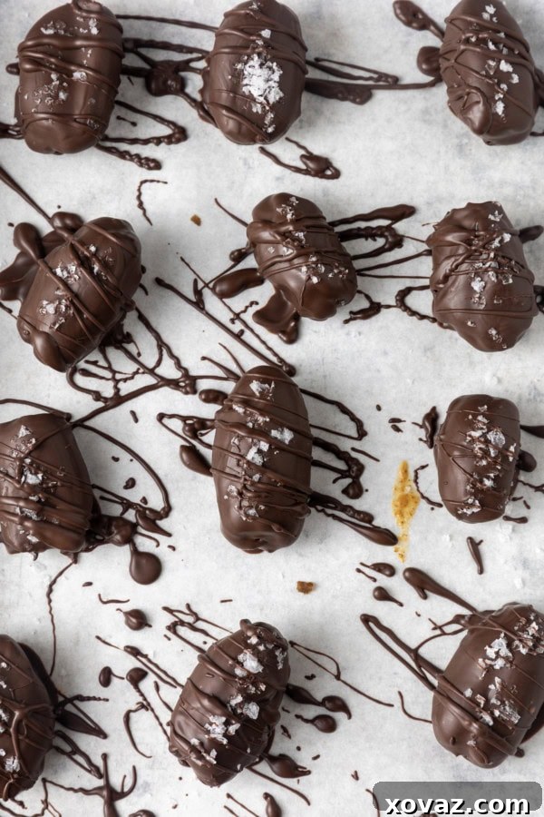 Close-up of chocolate covered almond stuffed dates with a dusting of sea salt on a parchment-lined sheet pan, showcasing their glistening chocolate coating.