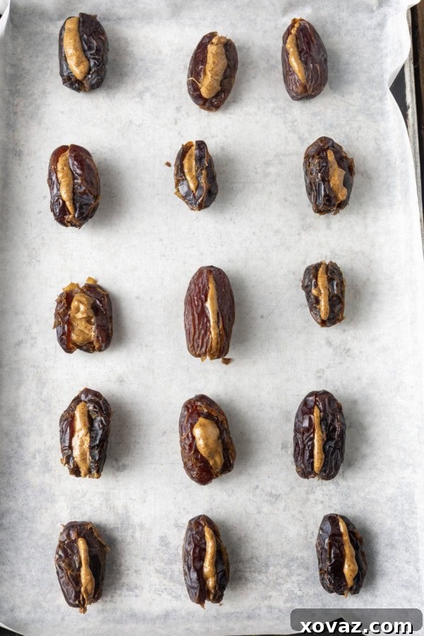 Almond butter stuffed Medjool dates, awaiting their chocolate coating, resting on a parchment-lined sheet pan with a light dusting of sea salt.
