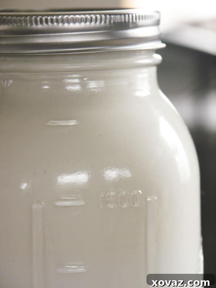 A glass jar filled with thick, creamy homemade cultured buttermilk, with a spoon resting in it.