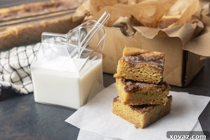 Cinnamon Sugar Snickerdoodle Bars 5 A hand reaching for a snickerdoodle cookie bar next to a glass of milk, emphasizing their enticing appearance.
