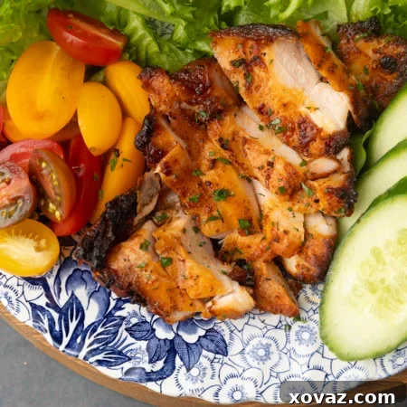 chicken thighs grilled on a pellet grill on a plate with lettuce, tomatoes, and cucumbers