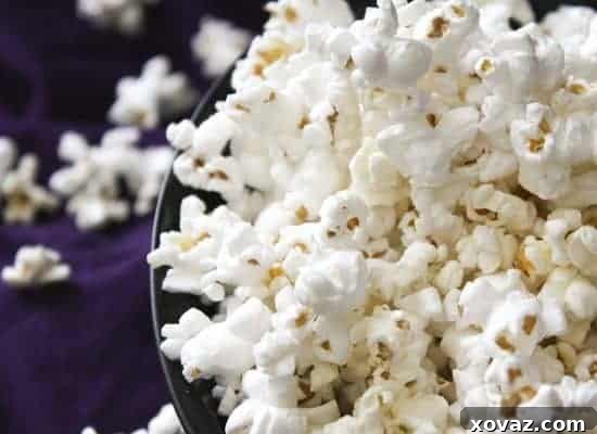 Classic salted stovetop popcorn in a white bowl with an old-fashioned popcorn maker in the background.