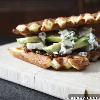 The King's Ultimate Waffle Sandwich Bacon Jam, Avocado and Gorgonzola 2 A delectable Bacon Jam, Avocado, and Gorgonzola Waffle Sandwich, served on a plate.