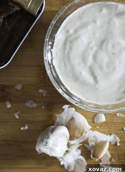 2-Minute Garlic Anchovy Mayonnaise Rich and creamy homemade garlic anchovy mayonnaise in a small white bowl, garnished with a fresh herb sprig.
