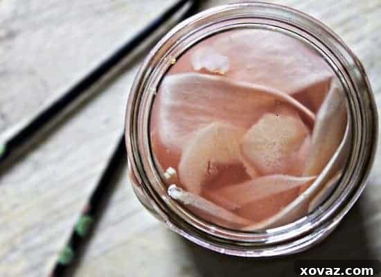 Freshly sliced homemade pickled ginger, vibrant pink, alongside a piece of sushi, showcasing its delicate texture.