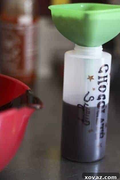 Closeup of homemade chocolate syrup being poured into a squeeze bottle, highlighting its smooth texture.