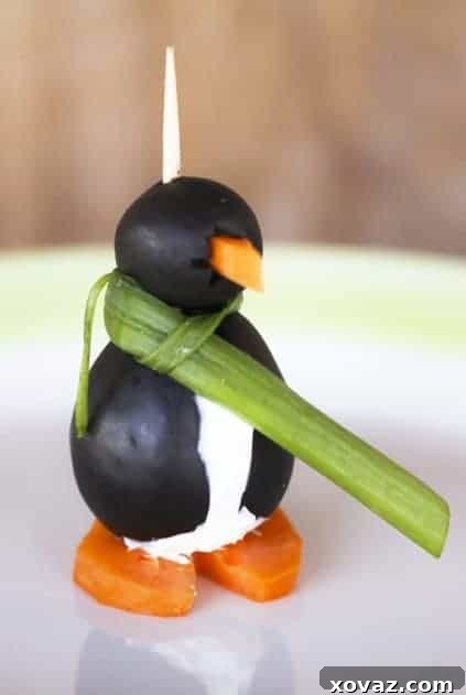 Adorable black olive penguins standing upright on a white plate, filled with creamy cheese, adorned with carrot beaks and feet. One penguin wears a green onion scarf.