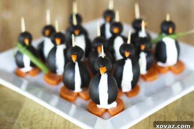 A charming display of assembled black olive penguins with cream cheese filling, carrot beaks and feet, some adorned with green onion scarves, arranged on a serving platter.