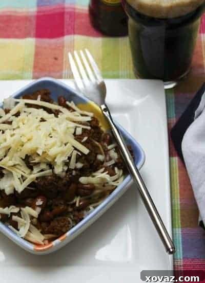 A generous serving of classic Cincinnati Chili with a mountain of shredded cheddar cheese, ready to be enjoyed