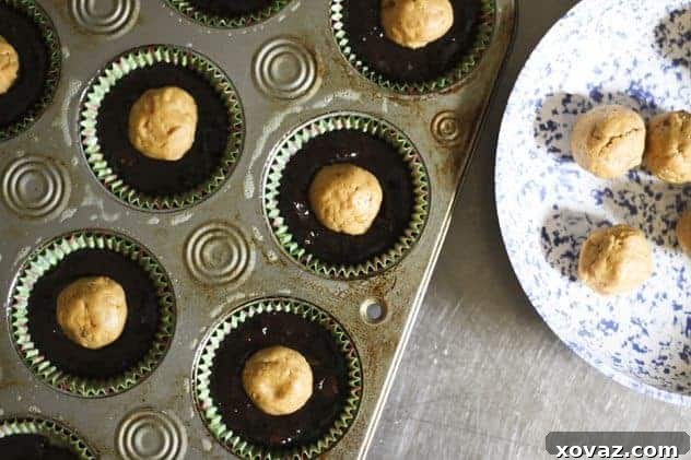 Brownie batter being scooped into muffin tins with peanut butter balls ready to be inserted.
